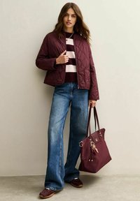 Burgundy quiltad jacka över en randig tröja, ihop med vida blå jeans och bruna sneakers. Brun handväska med guldförsedda detaljer.