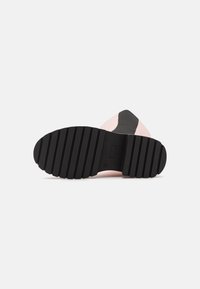 Suela de goma negra con surcos profundos, diseño superior en rosa y gris, punta afilada, materiales lisos y texturizados.