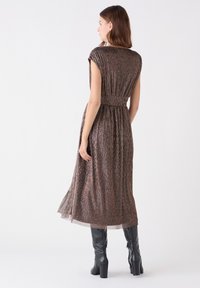 Middellange, bruine, gestructureerde jurk met kapmouwen, een ceintuur in de taille en een vloeiende rok; gedragen met zwarte kniehoge haklaarzen.