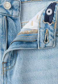 Jeans en denim bleu clair avec une fermeture éclair métallique dézippée, un bouton argenté et une ceinture élastique ajustable à l'intérieur de la ceinture.
