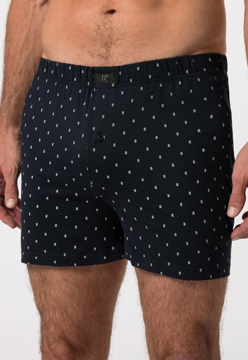 Černé boxerky vyrobené z měkké tkaniny, s vzorovaným designem a malými bílými čtverci, elastickým pasem a předním knoflíkovým uzávěrem.