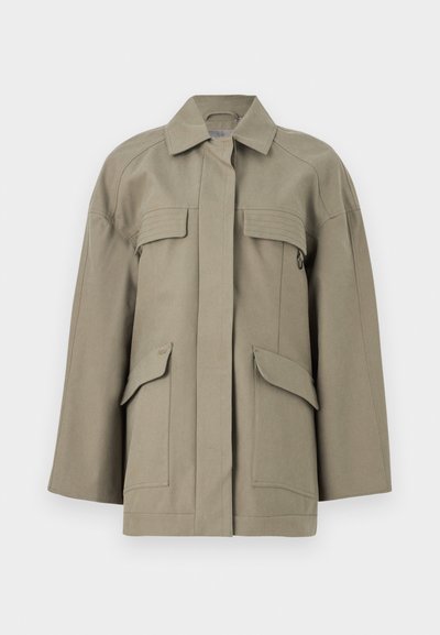 Μπεζ υπερμεγέθη μπουφάν με πλαϊνές τσέπες με καπάκι στο μπροστινό μέρος, κρυφό κούμπωμα με κουμπιά, φαρδιές μανσέτες και κλασικό γιακά σε λευκό φόντο.