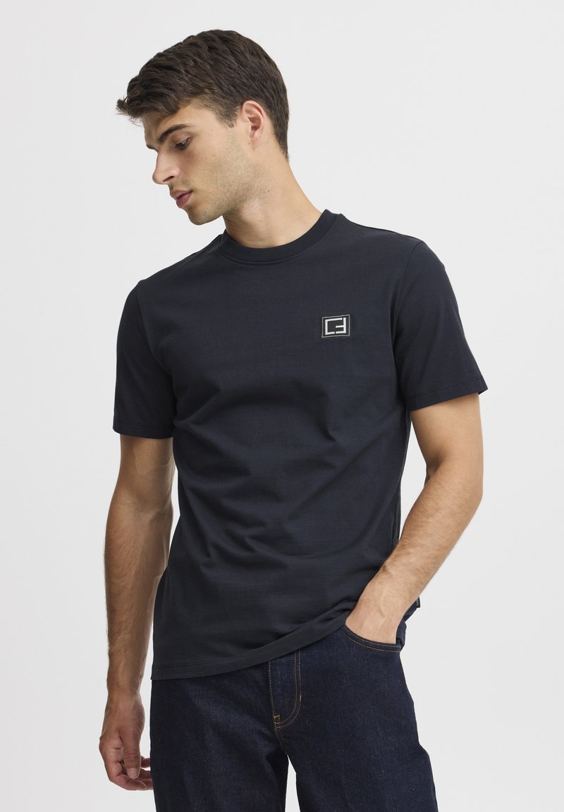 Tricou din bumbac bleumarin cu guler rotund și mâneci scurte, având un mic logo pătrat brodat pe pieptul stâng.