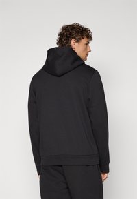 Sweat-shirt à capuche noir avec une texture lisse, présentant un design simple, un ourlet et des poignets côtelés, vu de dos. Pas de marque visible.