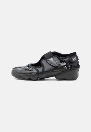 Čierna Nike Air obuv s suchým zipsom, zdobená malými čiernymi kvetinovými ozdobami na boku a vpredu.