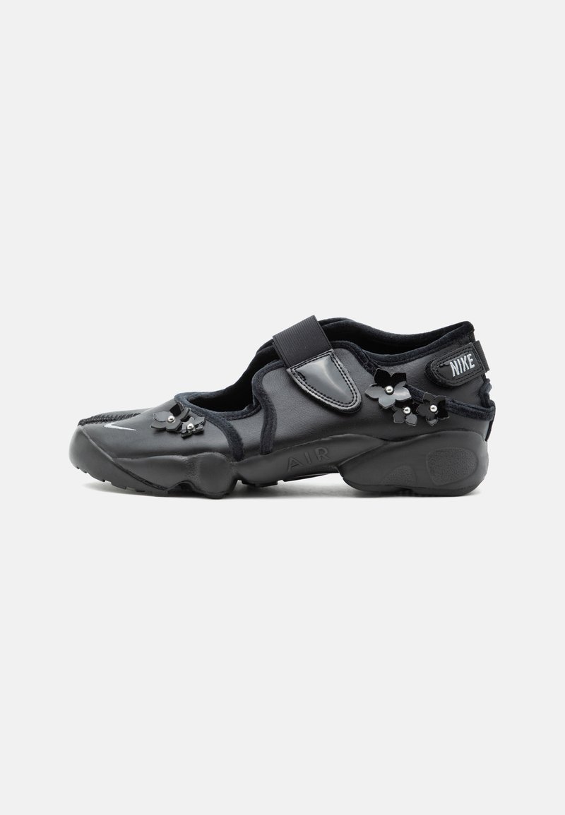 Μαύρο παπούτσι Nike Air με λουράκι βέλκρο, διακοσμημένο με μικρές μαύρες ανθισμένες διακοσμήσεις στο πλάι και στο μπροστινό μέρος.