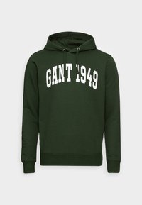 Felpa verde scuro con cappuccio regolabile, caratterizzata da un logo bianco "GANT 1949" in una forma curva che attraversa il petto. Tessuto morbido, polsini a coste.