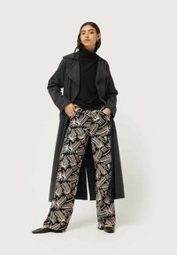 Largo abrigo negro sobre un cuello de tortuga negro, combinado con pantalones anchos de pierna ancha de patrón blanco y negro. Unos zapatos negros completan el atuendo.