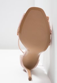 Escarpin en daim rose avec un bout pointu, un fin talon aiguille et une semelle texturée. Sangle à la cheville avec un détail décoratif.