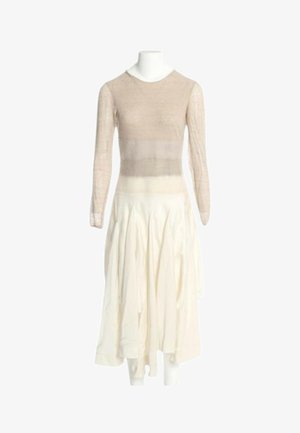 Top beige a maniche lunghe abbinato a una gonna fluente avorio a vita alta su un manichino bianco su uno sfondo semplice.