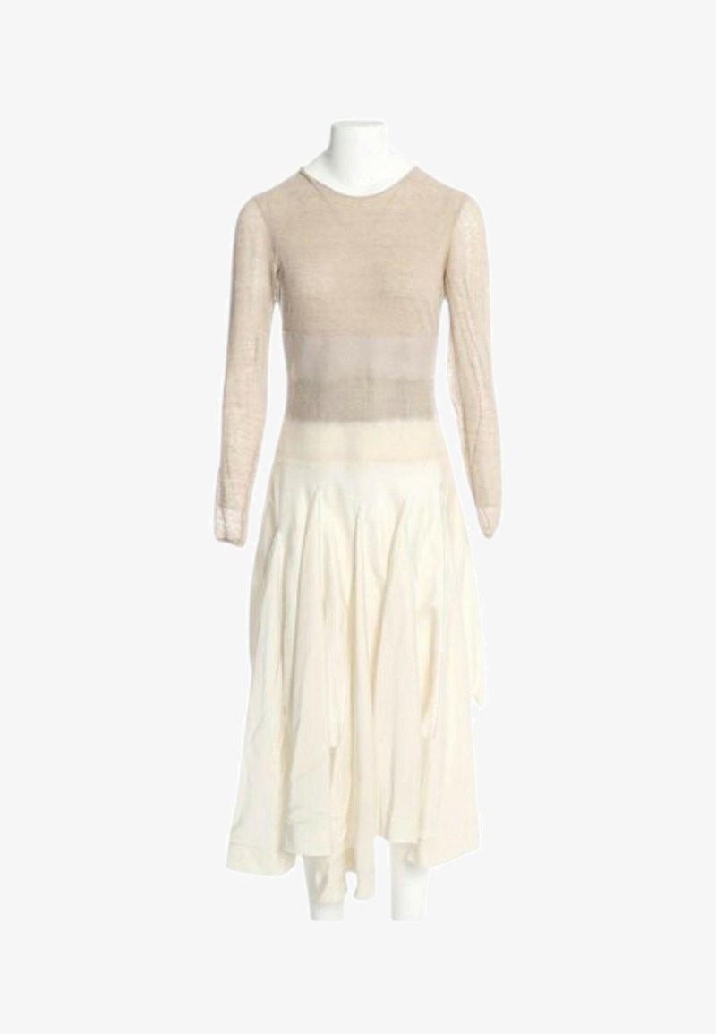 Haut beige à manches longues associé à une jupe fluide taille haute blanc cassé sur un mannequin blanc devant un fond uni.