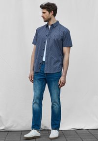 Korte mouwen navy-gepatenteerde shirt met een knoopsluiting aan de voorkant, gecombineerd met lichtblauwe jeans en witte sneakers. Soepele stof, casual pasvorm.