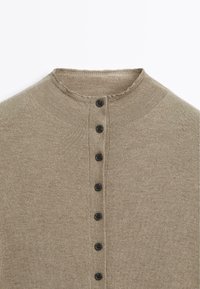 Cardigan beige en maille avec col rond et une rangée verticale de sept boutons noirs au centre devant.