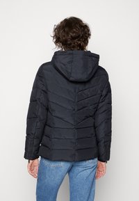 Schwarze Daunenjacke mit Kapuze, diagonal gestepptem Design, mit Reißverschluss an den Bündchen und einer leicht taillierten Silhouette.