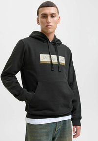 Sort hættetrøje lavet af bl�ødt materiale med en front kangaroo lomme, justerbare snore og et hvidt logo-patch med guld accenter.