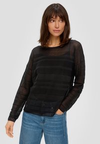Top nero a maniche lunghe con tessuto traslucido e texturizzato caratterizzato da strisce orizzontali. Girocollo e vestibilità rilassata, abbinato a jeans in denim blu chiaro.