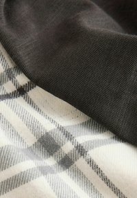 Schwarzer, strukturierter Stoff überlappt ein creme- und graumeliertes Karomuster. Die Linien sind scharf, wobei kontrastierende Farbblöcke visuelles Interesse erzeugen.
