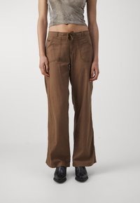 Bruna vida byxor gjorda av en texturerad tyg. Har en dragsko i midjan och stora framfickor. Matchat med svarta skor.