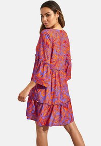 Paarse jurk met een oranje bloemenpatroon, vloeiende ontwerp, gerimpelde zoom en losse mouwen. Gemaakt van lichtgewicht stof.