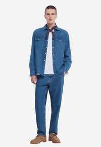 Jeansskjorta i medelblå färg med två bröstfickor, kombinerad med matchande blå jeans. Accessoarer inkluderar en mörk mönstrad scarf och bruna skor.