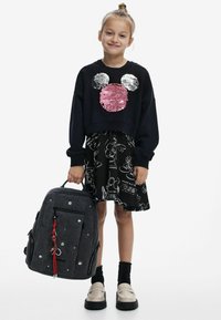 Schwarzes, gekürztes Sweatshirt mit Pailletten-Design von Mickey Mouse, kombiniert mit einem schwarzen Rock mit weißen Cartoon-Skizzen und einer grauen Umhängetasche.