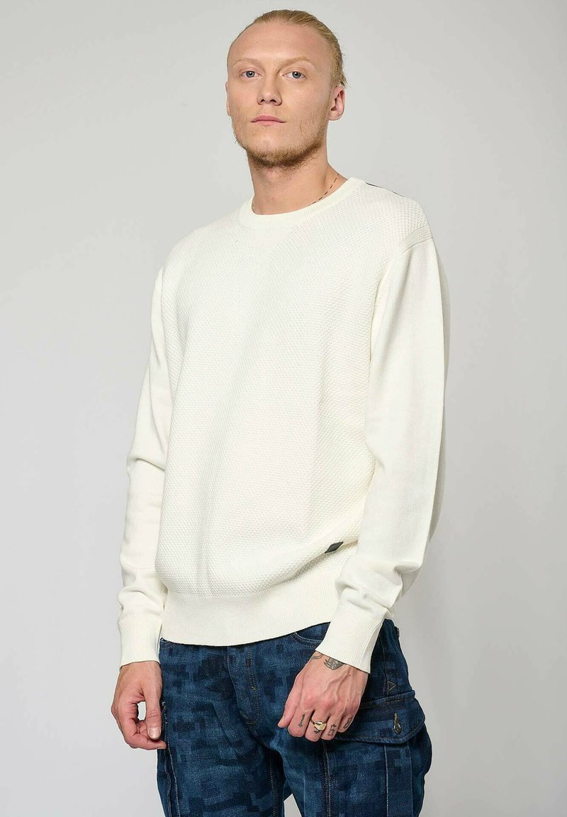 Witte textuurgebreide trui met lange mouwen, geribbelde manchetten en een losse pasvorm. Gekozen in combinatie met donkere cargo-broek met een patroon, met zichtbare stiksel-details.