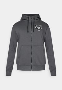Szara, zapinana na zamek bluza z kapturem, z kieszenią na przodzie, z regulowanym kapturem oraz logo Raiders na lewej piersi. Gładki materiał z ściągaczami przy mankietach i dolnej krawędzi.