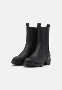 Bottes noires à talons en cuir avec des panneaux latéraux élastiques, bout rond, semelle texturée et un petit accent doré sur le talon.