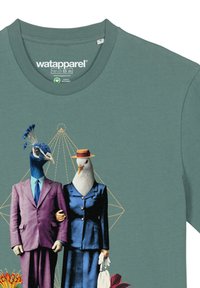 Groene T-shirt met een grafisch ontwerp van een pauw in een paarse pak en een meeuw in een blauwe outfit, met abstract geometrische patronen op de achtergrond.