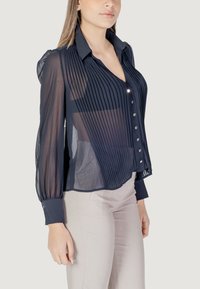 Navyblauwe, doorschijnende blouse met verticale plooien, knoopsluiting aan de voorkant en lange mouwen met manchetten. Heeft glanzende knopen en een kraag.