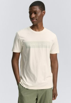 Cremefarvet kortærmet t-shirt lavet af blødt stof, med et trykt "DENIM TOM TAILOR" logo i et afdæmpet grønt rektangel på forsiden.