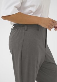 Pantalons gris ajustés avec une texture lisse, une taille élastique et des poches latérales. Le tissu présente un motif subtil.