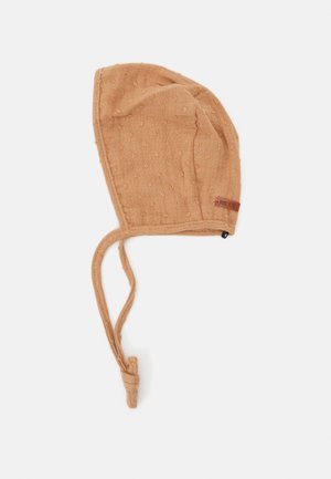 Boné de bebé em algodão bege, texturizado com pequenos pontos elevados, apresenta fitas para um ajuste seguro, com um rótulo de logo na lateral.