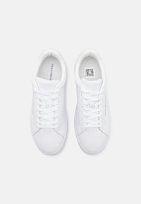 Zapatillas deportivas blancas con un upper de cuero suave, cierre de cordones, cuello acolchado y un logo sutil en el lateral y la lengüeta.