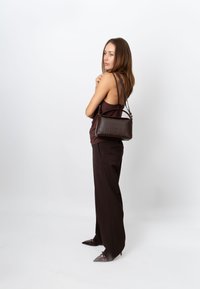 Geantă de mână maro din piele cu o formă dreptunghiulară bine definită, cu un model texturat subtil și două bretele pentru umăr. Purtați cu pantaloni închiși la culoare și pantofi cu vârf ascuțit.