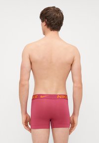 Nike muške bokserice, bordo tkanina, elastični pojas s narančastim Nike logotipom, uski dizajn, glatka tekstura, dužina do sredine buta.