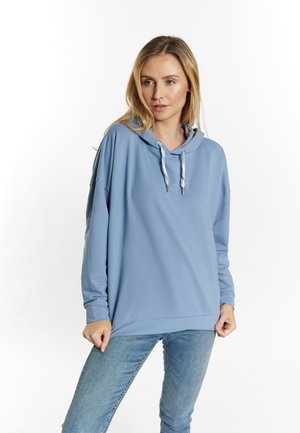 Hellblaues Kapuzensweatshirt mit lockerer Passform, ausgestattet mit einem Kordelzug, langen Ärmeln und einer glatten Textur. Kombiniert mit blauen Jeans.