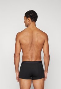 Caleçons de boxe noirs avec une finition lisse et une taille douce, vus de dos sur une personne avec une silhouette musculaire.