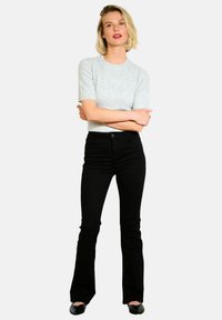 Top gris de manga corta combinado con pantalones negros ajustados de campana. Los pantalones cuentan con un cierre de botón y un ligero estiramiento. Textura de tela suave en toda la prenda.