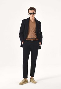 Meresinine kahekaraline mantel, pruun soonikkoes kampsun, mustad püksid, beež vöö ja paeltega beežad tossud. Stiili täiendab päikeseprillid.