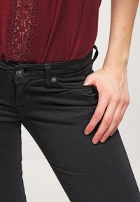 Burgundy topp med spetsdetaljer, kombinerad med svarta åtsittande jeans. Jeans sträcker sig med en framficka och har en jämn yta.