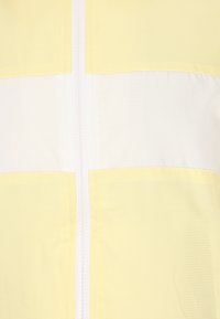 Giacca zip-up gialla e bianca con texture a griglia, caratterizzata da una cerniera centrale e un design a blocchi di colore. Tessuto leggero.