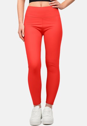 Leggings rouges avec une texture lisse et extensible, ainsi qu'une taille haute, assortis à des baskets de sport blanches.