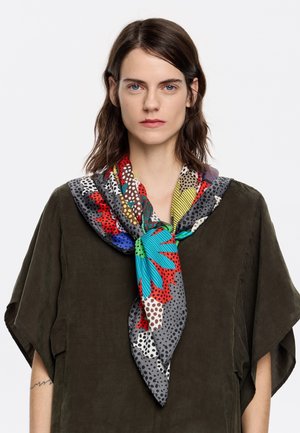 Foulard di seta colorato con motivi floreali e pois blu, rossi e gialli, annodato in modo ordinato attorno al collo.