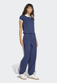 Tamnoplava kratka majica s bijelim ovratnikom, uparena s širokim tamnoplavim hlačama s bijelim bočnim prugama. Bijele tenisice zaokružuju izgled.