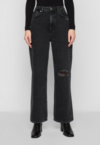 Svarta högmidjade vida jeans i denimtyg, med rivna knädetaljer och sidofickor. Matchas med svarta klackboots.