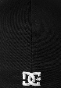 Gorra negra con un distintivo logotipo de DC bordado en blanco y un acento de estrella. El material tiene un acabado texturizado con costuras visibles.