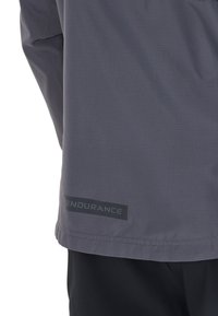 Graue Sportjacke mit strukturiertem Finish, ausgestattet mit einem schwarzen "ENDURANCE"-Logo am Saum, entworfen für aktive Freizeit.