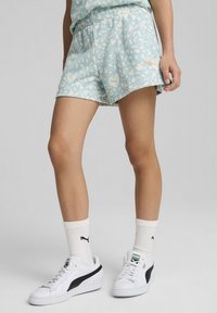 Shorts bleu clair avec un motif floral, taille élastique et accent logo doré. Associés à des baskets blanches et des chaussettes blanches à côtes.