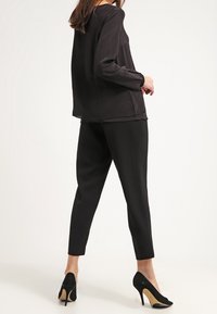 Svart silkesblus med långa ärmar och rundad halsringning, matchad med skräddarsydda svarta byxor och svarta högklackade skor.